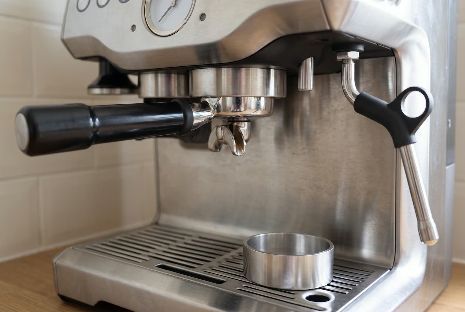 A close view of an espresso machine's group head with a portafilter locked in beside its steam wand.
