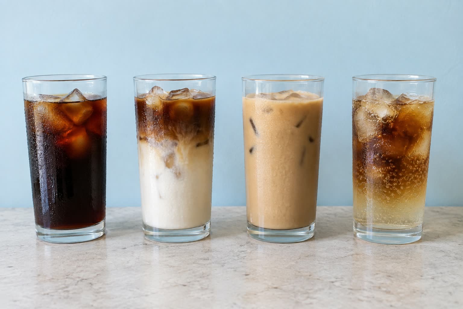 Four tall plain glasses of iced coffee stand in a row on a pale stone counter in front of a pale blue wall, one black over ice, one with a dark layer sitting on milk, one fully mixed and pale, and one pale amber and fizzing with a dark layer settling through it.
